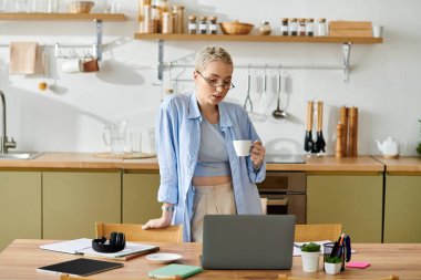 Işıl ışıl parlayan alanda, kısa saçlı genç bir kadın çalışırken kahvesinin tadını çıkarıyor..