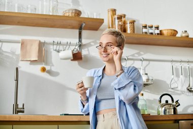 Genç bir kadının neşeli bir gülümsemeyle içkisinin tadını çıkardığı parlak ve havadar bir mutfak..