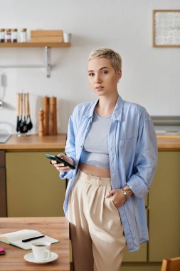 Samimi bir mutfakta, kısa saçlı genç bir kadın telefonuyla meşgul, güzel ve dengeli..