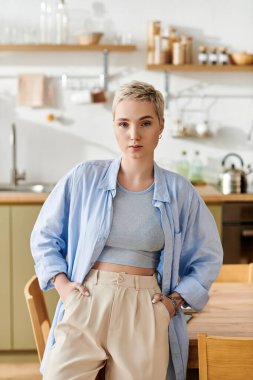 Evde dinlenen, kısa saçlı genç bir kadın, günlük kıyafetlerini giyerken güzellik ve güven saçar..