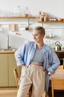 Samimi bir mutfakta, kısa saçlı genç bir kadın şık kıyafetler içinde rahatlıyor..