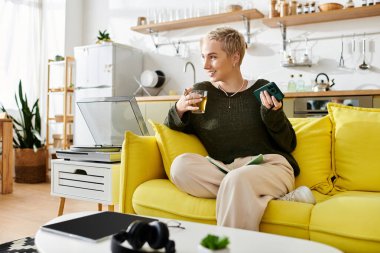 Genç bir kadın sarı bir kanepede dinleniyor, elinde içki, parlak, davetkar bir odada..