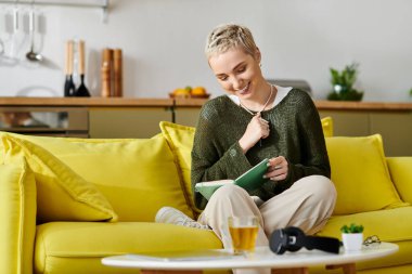 Neşeli bir kadın sarı bir kanepede dinleniyor, evdeki bir kitaba dalmış..