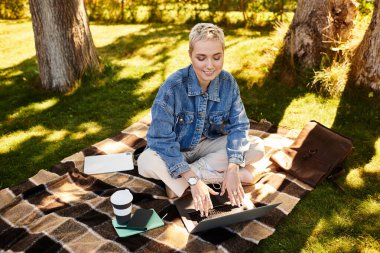 Kısa saçlı genç bir kadın huzurlu bir açık havada geziniyor, doğayı takdir ediyor..