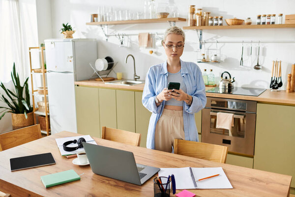 A beautiful young woman with short hair stands in her cozy kitchen, focused on her phone.