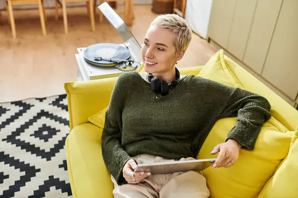 Sarı bir kanepeye gülümseyen genç bir kadın, rahatlatıcı ve tabletiyle meşgul..