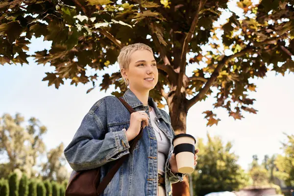 Kısa saçlı neşeli genç bir kadın açık havada yürüyor, güneşin altında bir içkinin tadını çıkarıyor..