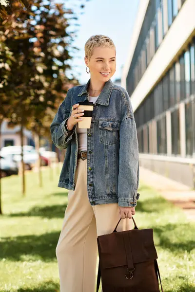 Parlak güneş ışığı, kısa saçlı genç bir kadını aydınlatıyor. Yürürken neşeyle kahveyi yudumluyor..