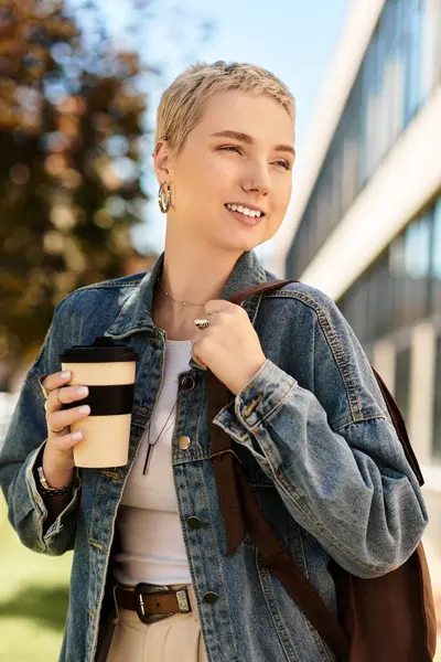 Kısa saçlı genç bir kadın dışarıda mutlu mesut dolaşıyor, kahvesinin ve güneşinin tadını çıkarıyor..