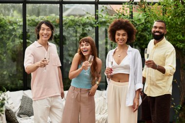 Şık gündelik kıyafetler içindeki mutlu arkadaşlar canlı bir açık hava kafede birlikte kutluyor, neşeyi paylaşıyorlar..