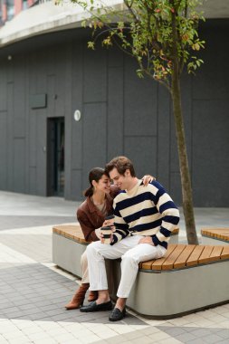 Mutlu bir çift, canlı bir şehir manzarasının ortasında kahkahalarla bir bankta kahkaha atıyor..