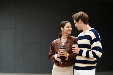 Çift birbirine yakın duruyor, gülümsüyor ve kahveyi paylaşıyor, modern bir ortamda aşk yayıyor..