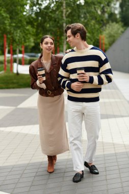 Neşeli genç bir çift parkta geziniyor, kahvelerini yudumluyor ve birlikte eğleniyorlar..