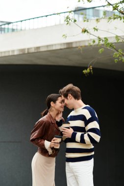 Neşeli genç bir çift, yakın durup, sıcak içecekler içiyorlar, şehirde birbirlerinin varlığından keyif alıyorlar..