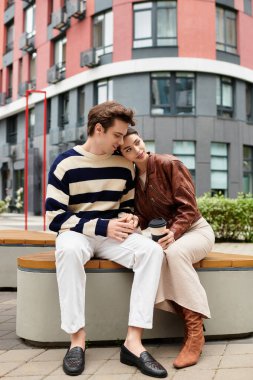 Genç bir çift, canlı bir şehir meydanında bir bankta birbirine eşlik etmekten zevk alır..