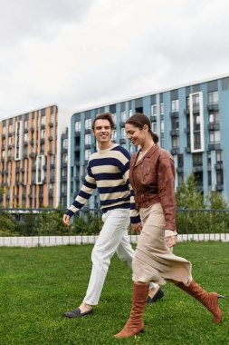 Genç bir çift, modern mimarinin yeşil parkında el ele dolaşır..