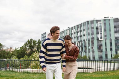 Genç bir çift, hayat dolu bir parkta yürürken kahkaha ve şefkat paylaşıyor..