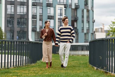 Genç bir çift el ele yürür, gülümseyerek ve parkta birbirlerine eşlik ederek eğlenirler..