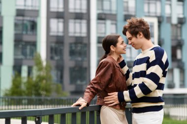 İki genç aşık birbirlerini kucaklıyor, gülümsüyor ve neşeyi çağdaş bir şehrin arka planında paylaşıyorlar..