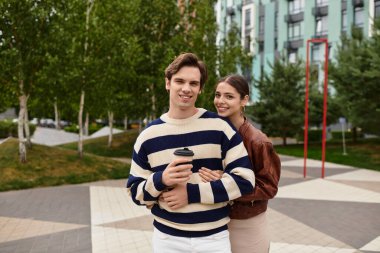 Genç bir çift, doğayla çevrili kahvenin tadını çıkarırken şefkatli bir kucaklaşmayı paylaşıyor..