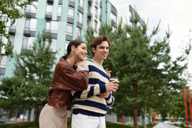 Genç bir çift birbirine yakın duruyor, kahvenin tadını çıkarıyor ve canlı bir park alanında sevgi dolu bir kucaklaşmanın tadını çıkarıyor..