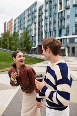 Genç çift, canlı bir şehirde el ele yürürken kahkaha ve şefkat paylaşıyor..