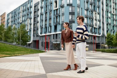 Sevgi dolu çift el ele yürür, çağdaş binalar ve yeşil alanlar arasında kahkahalar paylaşır..