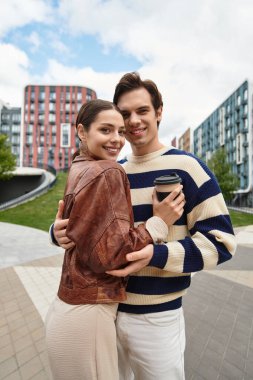 Sevgi dolu bir çift, canlı bir şehir ortamında kahvelerini yudumlarken sıcak bir şekilde kucaklaşır..