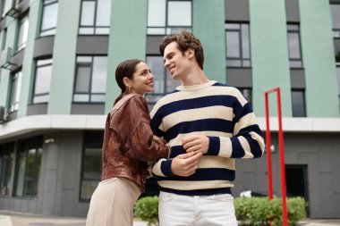 Genç bir çift birbirine gülümsüyor, canlı bir şehirde sıcak bir kucaklaşmayı paylaşıyor..