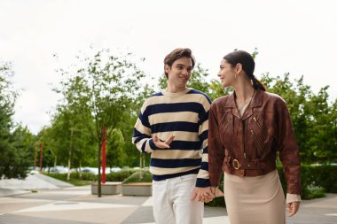 Genç bir çift yeşil bir parkta el ele dolaşır, gülümsemelerini ve neşelerini paylaşır..