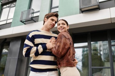 Sevgi dolu bir çift gülümser ve sıcak bir şekilde kucaklaşır. Sevgisini şık bir şehirde gösterir..