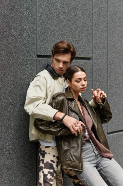 Çift, modern bir mekanda şık bir duvara yaslanırken birbirlerinin varlığından zevk alır..