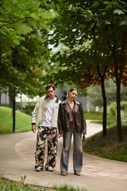 Neşeli bir çift, yemyeşil ve ağaçlarla çevrili dolambaçlı bir yolda birlikte yürüyor..