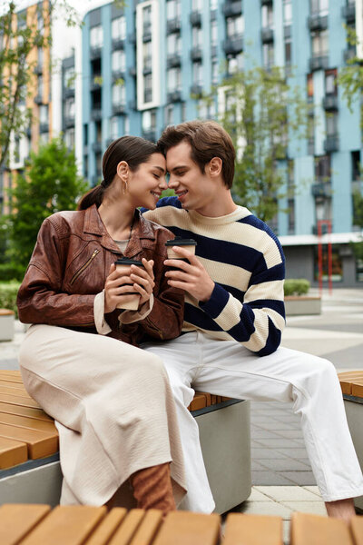 Любящая пара сидит рядом на скамейке, улыбаясь и наслаждаясь теплыми напитками на открытом воздухе в городе