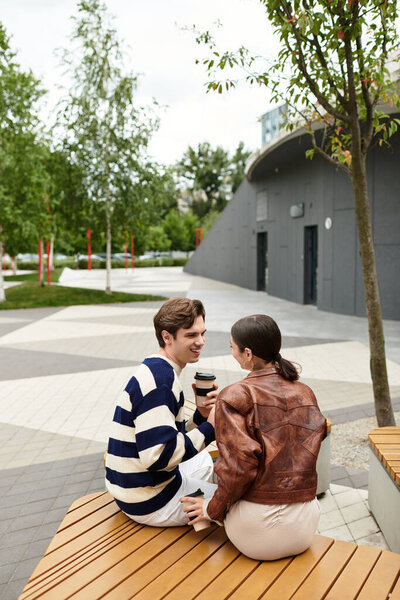 Молодая пара сидит на деревянной скамейке, наслаждаясь компанией друг друга в парке.