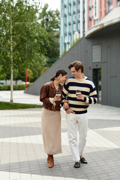 Любящая пара гуляет рука об руку, потягивая вместе кофе на оживленной городской площади.