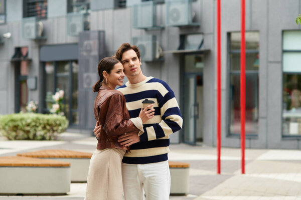 A young couple shares a warm embrace and joy over coffee in a modern outdoor space.