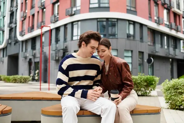 İki genç aşık yakın bir bankta oturuyor, sıcaklığını ve bağlantısını modern bir kentsel alanda paylaşıyorlar..
