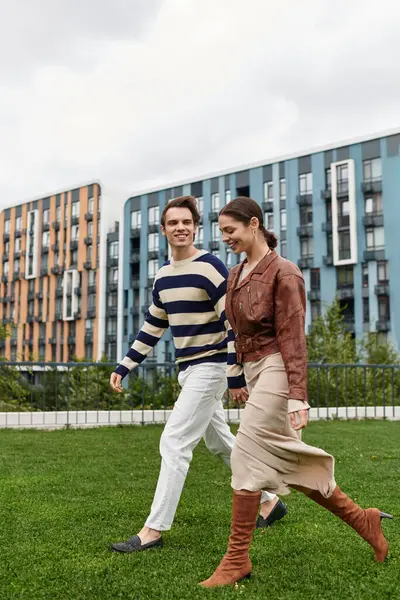 Genç bir çift, modern mimarinin yeşil parkında el ele dolaşır..