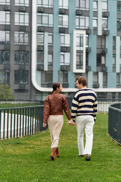 Sevgi dolu çift, çağdaş binaların yakınındaki canlı yeşil bir alanda el ele yürüyor..