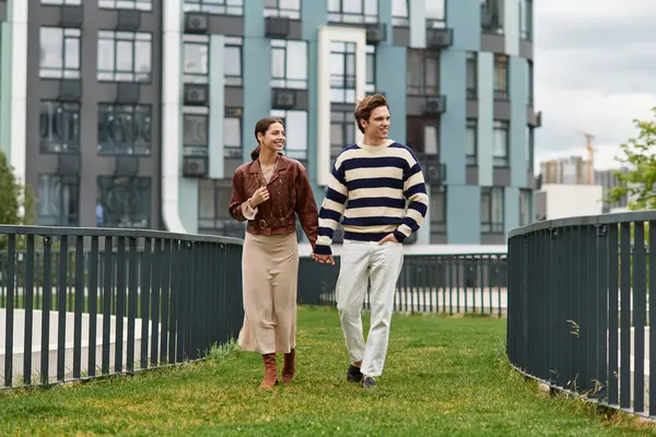 Genç bir çift el ele yürür, gülümseyerek ve parkta birbirlerine eşlik ederek eğlenirler..