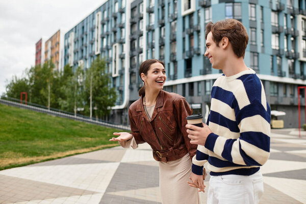 Пара идет рука об руку, смеясь и выпивая кофе в оживленном городском пейзаже.