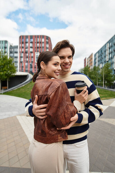 Молодая пара обнимается с радостью, разделяя тепло и смех среди современных зданий и природы.