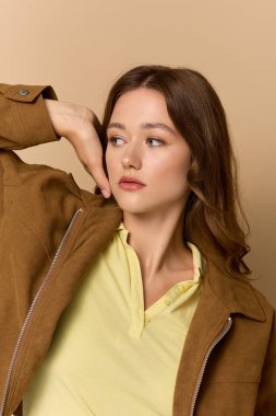 Sarı bir kıyafet ve kahverengi ceket içinde zarif bir şekilde poz veren genç bir kadın..