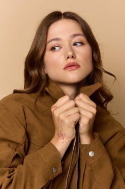Güzel genç bir kadın, modaya uygun kahverengi bir ceketle rahatça poz veriyor..