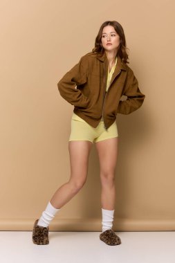 Genç bir kadın, sonbahar modasını şık sarı bir elbise ve kahverengi bir ceketle sergiliyor..