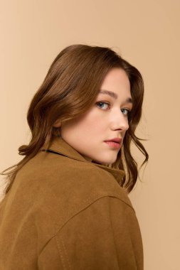 Güzel genç bir kadın şık kahverengi bir ceketle rahatça poz verir..