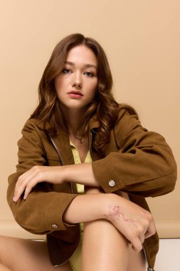 Güzel genç bir kadın şık sarı bir elbise ve kahverengi bir ceket içinde şık bir şekilde poz veriyor, sonbahar havası yayıyor..