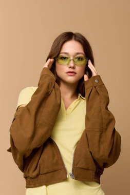 Genç bir kadın bej renkli bir stüdyoda poz veriyor, şık bir sonbahar kıyafetleri ve canlı renkleri var..