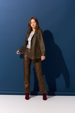 Güzel, genç bir kadın kahverengi deri bir elbise içinde poz veriyor. Stüdyoda sonbahar modasını somutlaştırıyor..